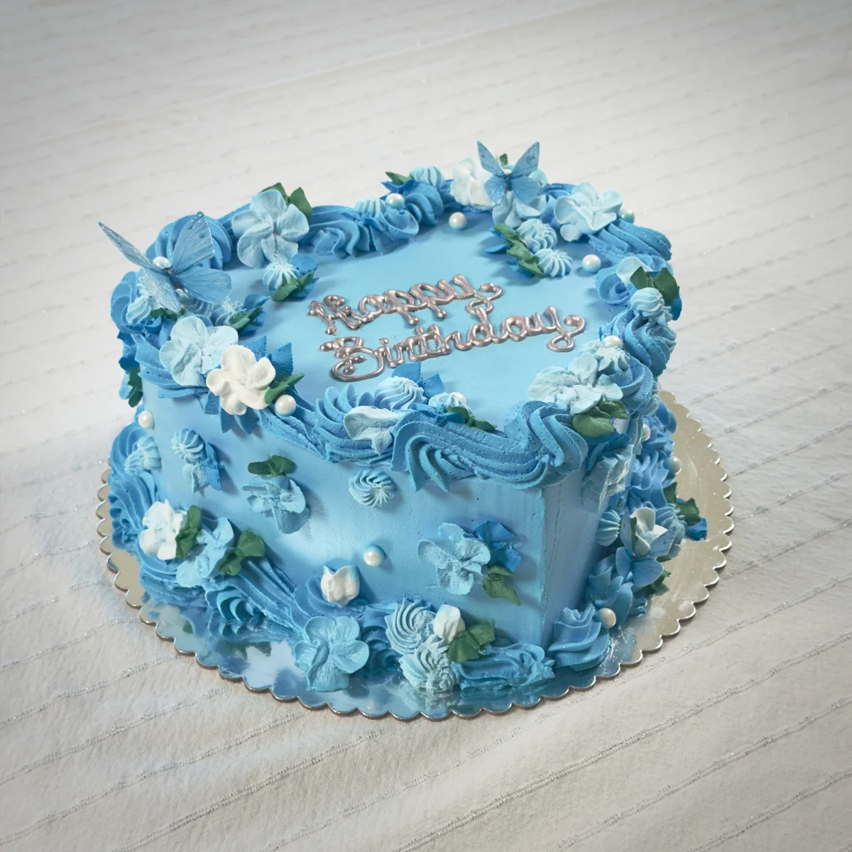 Blue heart-shaped birthday cake with buttercream flowers, pearls and butterflies